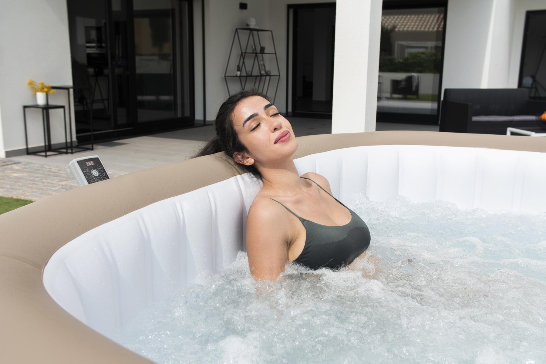 A woman unwinds in a large square inflatable Lay-Z-Spa Palma Hydrojet Pro hot tub, embracing relaxation in a cosy outdoor space. 